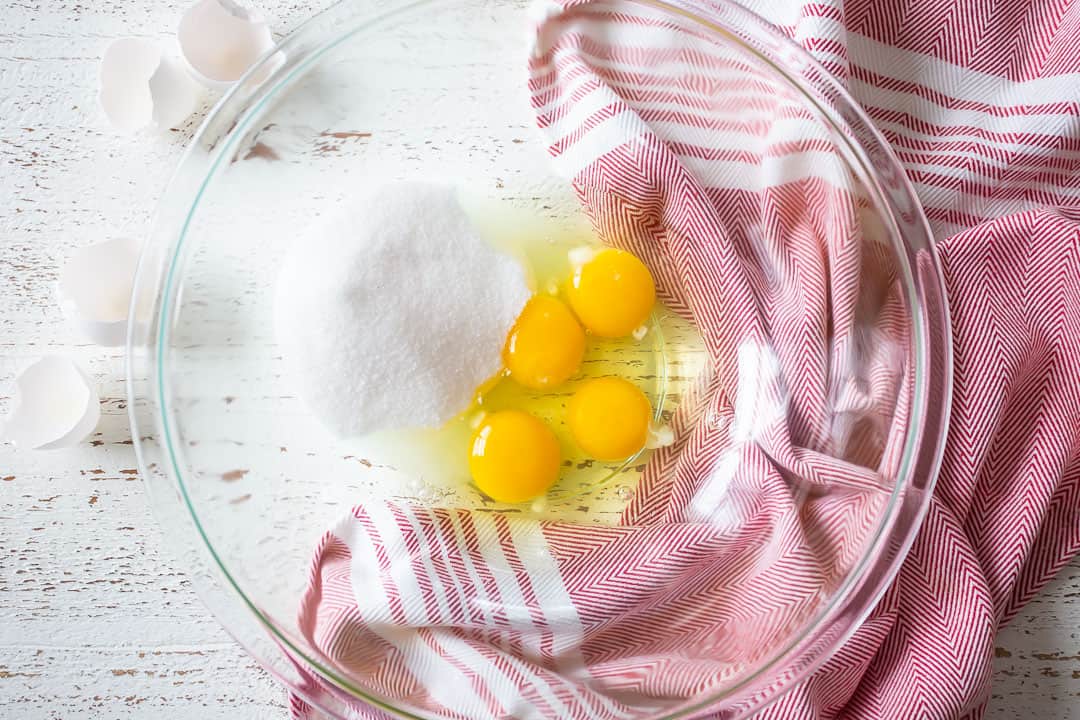Eggs and sugar in a large glass mixing bowl.
