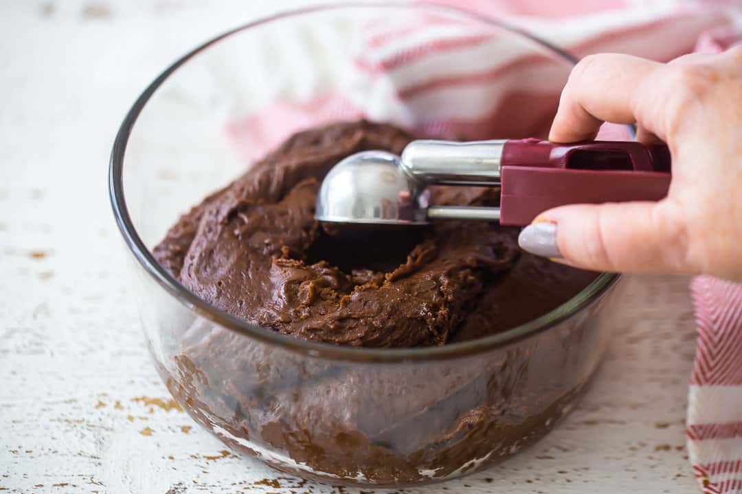 Shaping chocolate crinkle cookie dough with a cookie scoop.