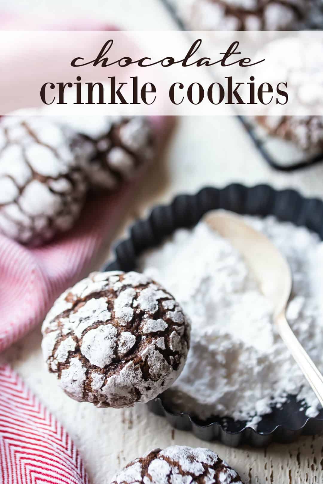 Chocolate crinkle cookies on a dish of powdered sugar with a vintage silver spoon and a text overlay above reading "Chocolate Crinkle Cookies."