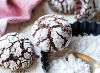 Chocolate crinkle cookies with a dish of powdered sugar and a red kitchen towel.