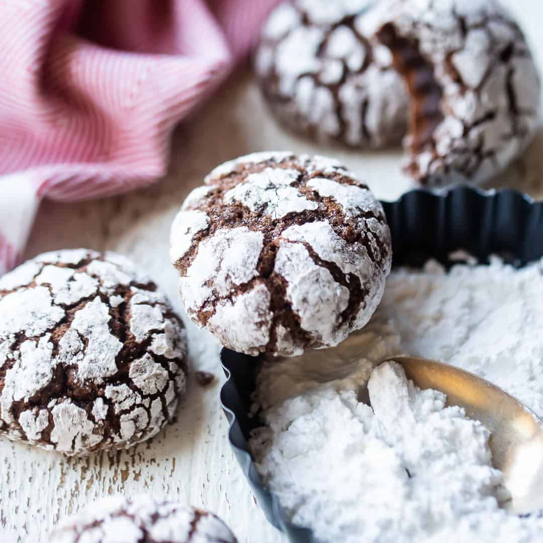 Chocolate crinkle cookies with a dish of powdered sugar and a red kitchen towel.