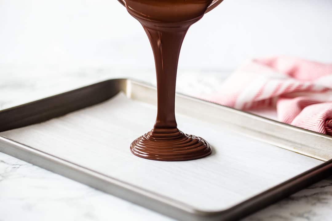Pouring melted chocolate onto a parchment-lined baking sheet.