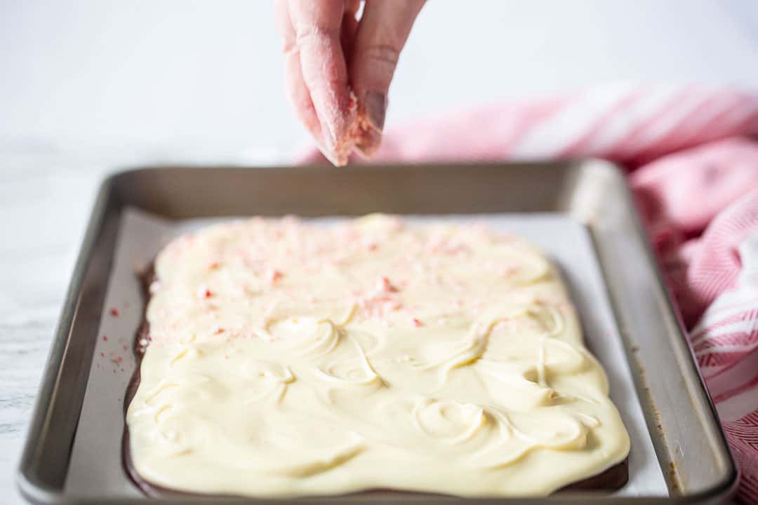 Sprinkling crushed candy canes over best peppermint bark recipe.