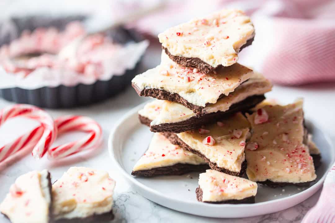 Peppermint bark recipe, prepared and stacked on a white plate with a red cloth in the background.