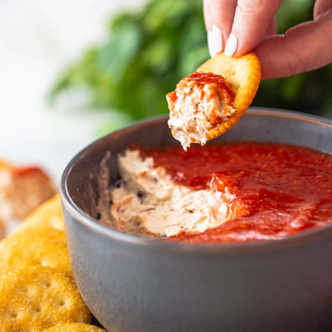 Scooping crab dip from a bowl with a cracker.