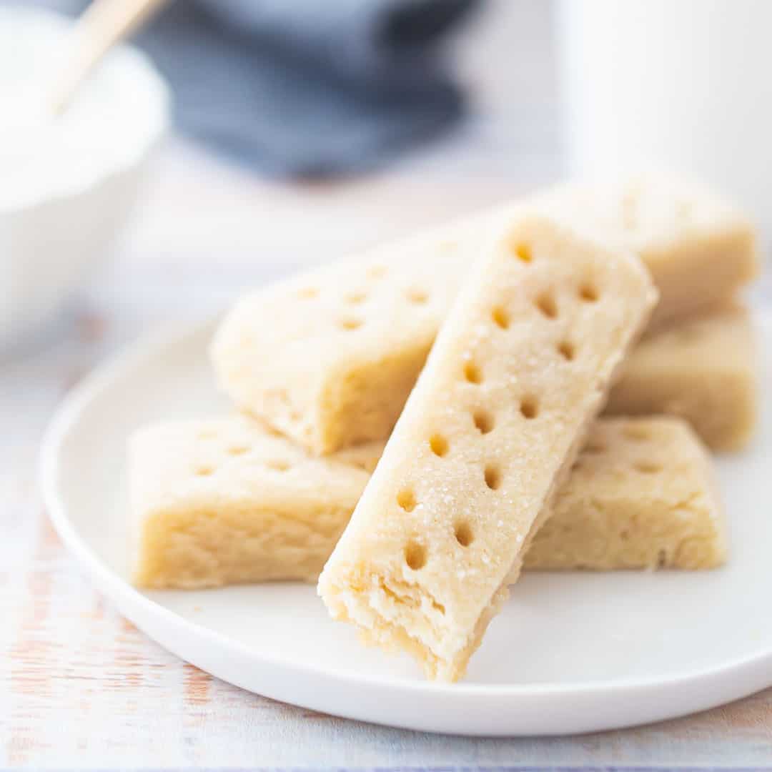 Shortbread cookies on a white plate with a sugar bowl in the background.