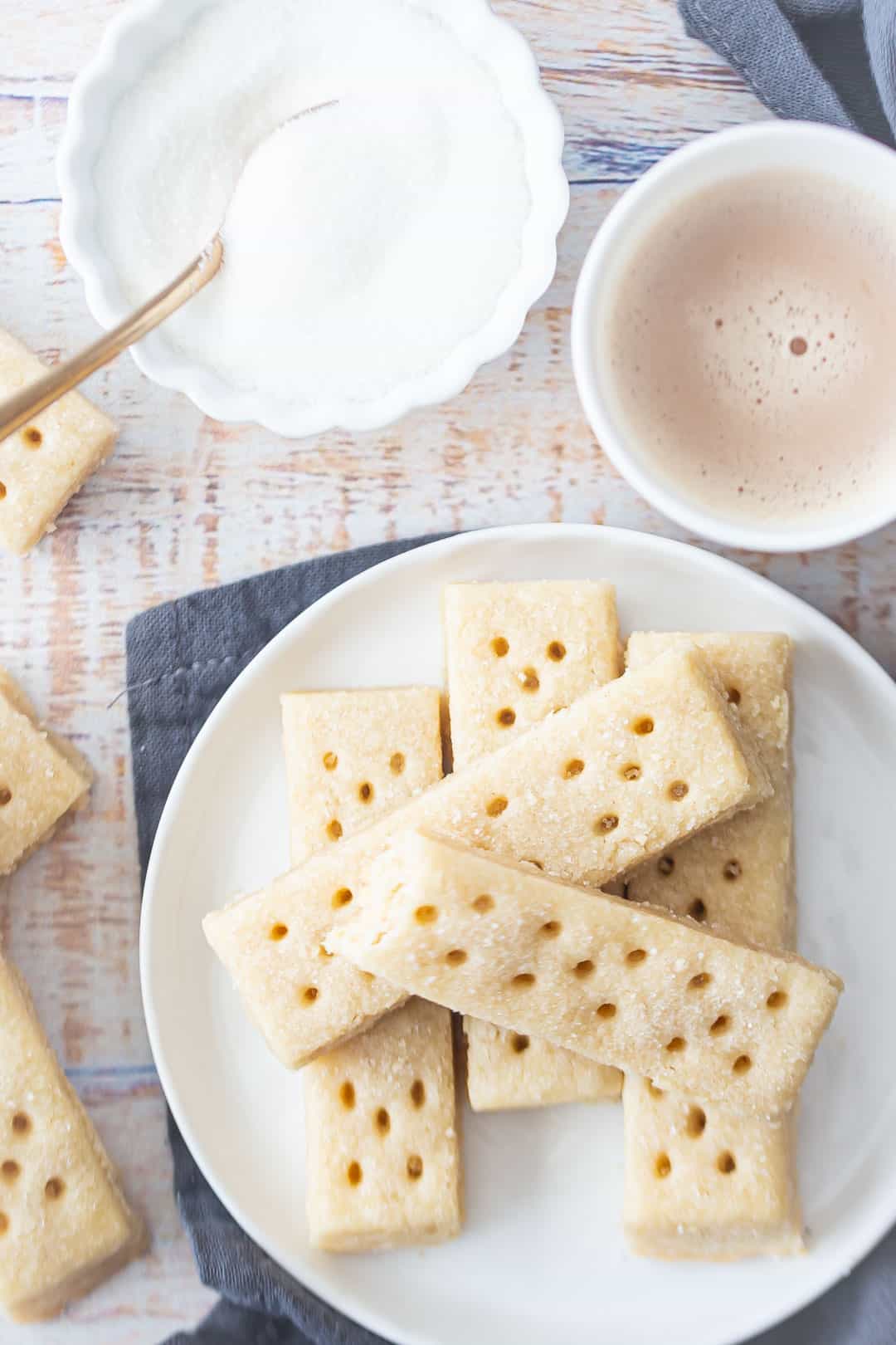Overhead image of shortbread cookies for Christmas, on a plate with a gray napkin and a cup of tea.