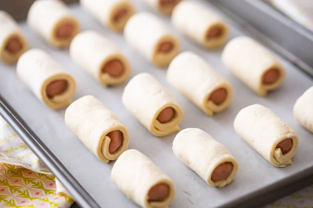 Unbaked pigs in a blanket on a parchment-lined baking sheet.