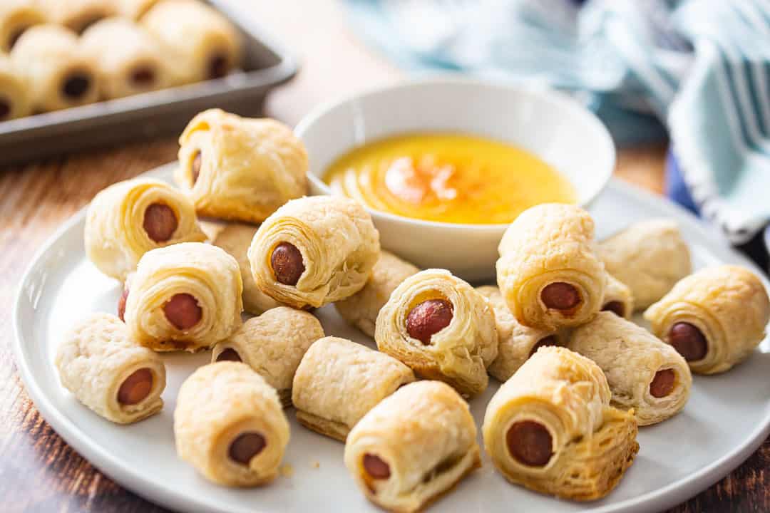 Pigs in a blanket, from scratch, arranged on a serving platter with a small bowl of honey mustard sauce.