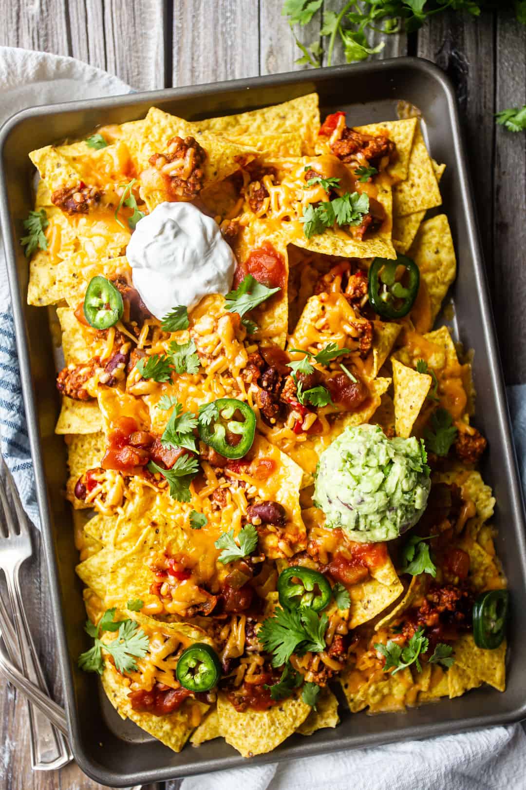 Overhead image of sheet pan nachos with chili, cheese, salsa, jalapenos, guacamole, sour cream, and cilantro.