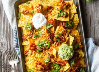 Overhead image of nachos on a sheet pan with forks and fresh cilantro.