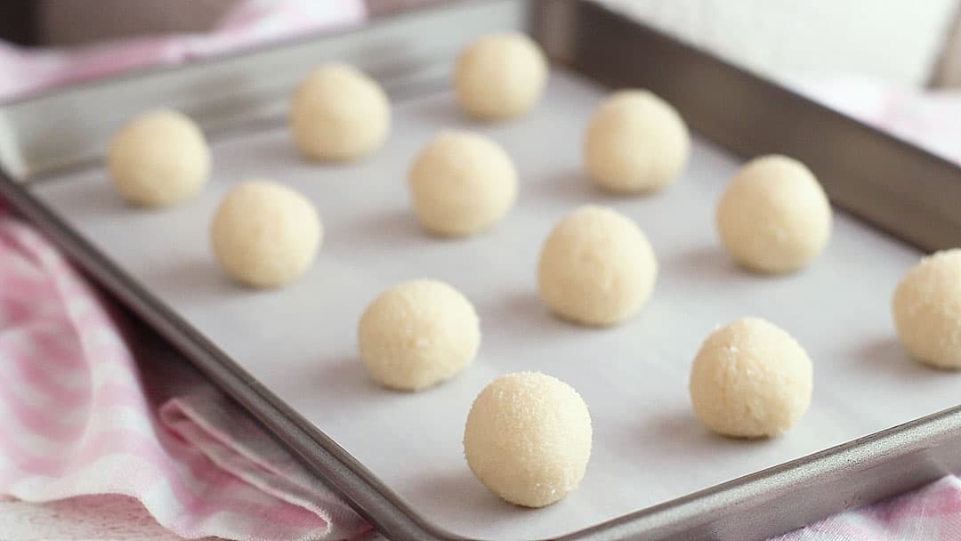 Thumbprint cookie dough balls on a baking sheet.
