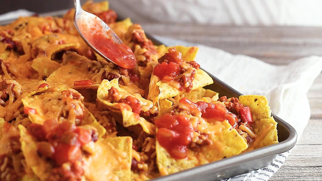Spooning salsa over sheet pan nachos recipe.