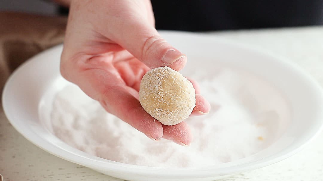 Rolling peanut butter blossoms dough balls in sugar.