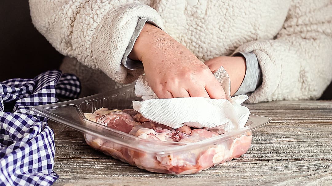 Patting raw chicken wings dry with paper towels.