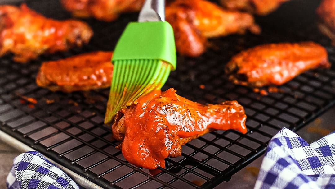 Brushing spicy buffalo sauce onto crispy baked chicken wings.