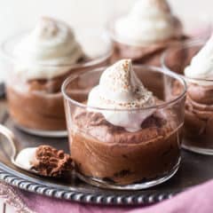 Small glass bowls of chocolate mousse with whipped cream on an antique silver tray.