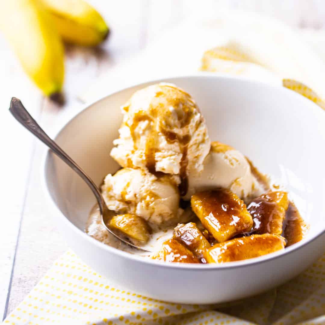 Bananas Foster in a white bowl with vanilla ice cream.