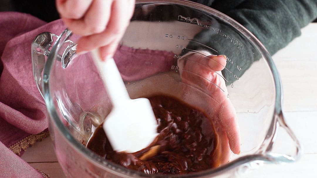 Stirring melted chocolate mousse ingredients together until smooth.