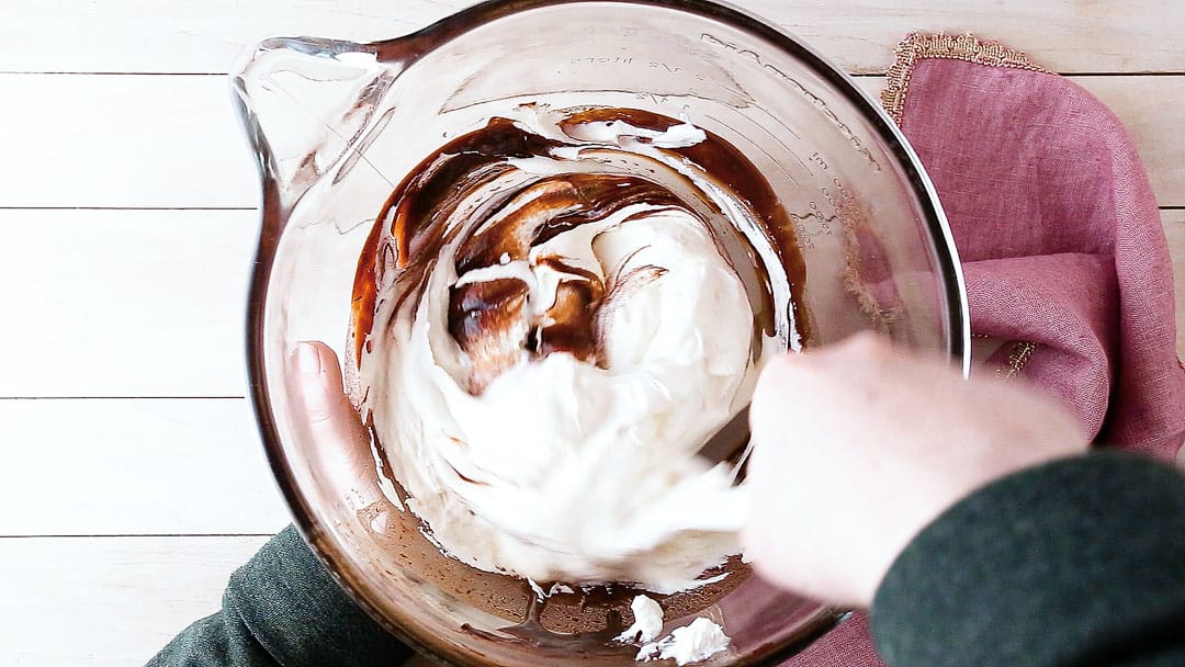 Folding stiffly whipped cream into chocolate mousse.