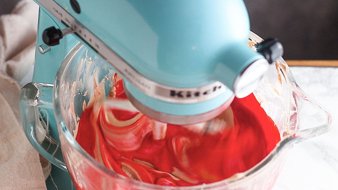 Red velvet cheesecake batter in a blue stand mixer.