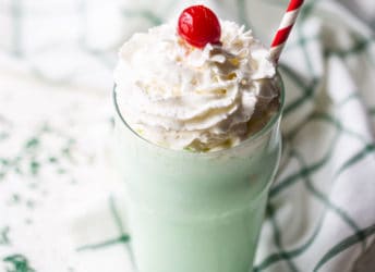 Shamrock shake in a tall glass with whipped cream and a cherry on top.
