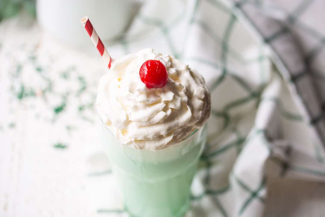 Shamrock shake served with whipped cream, a cherry, and a red striped straw.