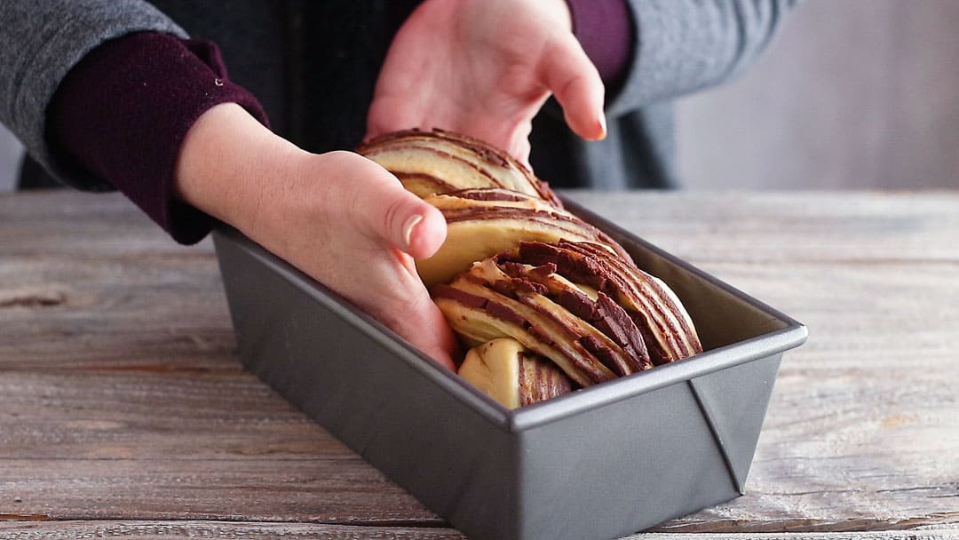 Placing chocolate babka in a loaf pan.