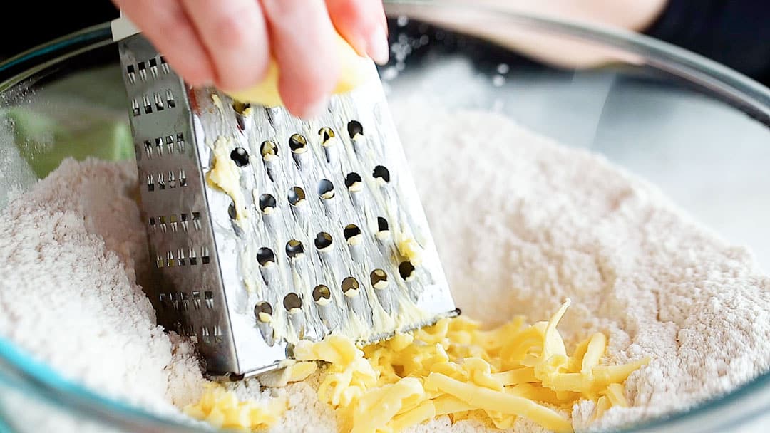 Grating cold butter into dry ingredients to make scones.