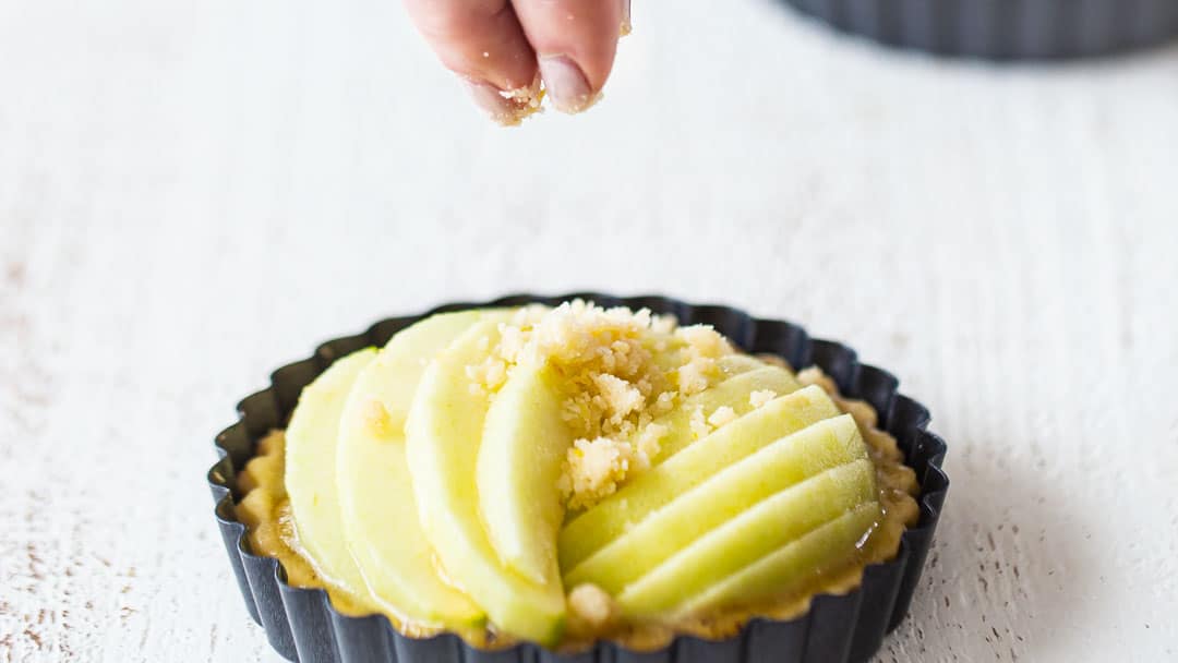 Sprinkling crumb topping over unbaked apple tarts.