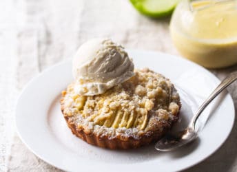 Apple tart with crumb topping on a white plate with a scoop of vanilla ice cream.