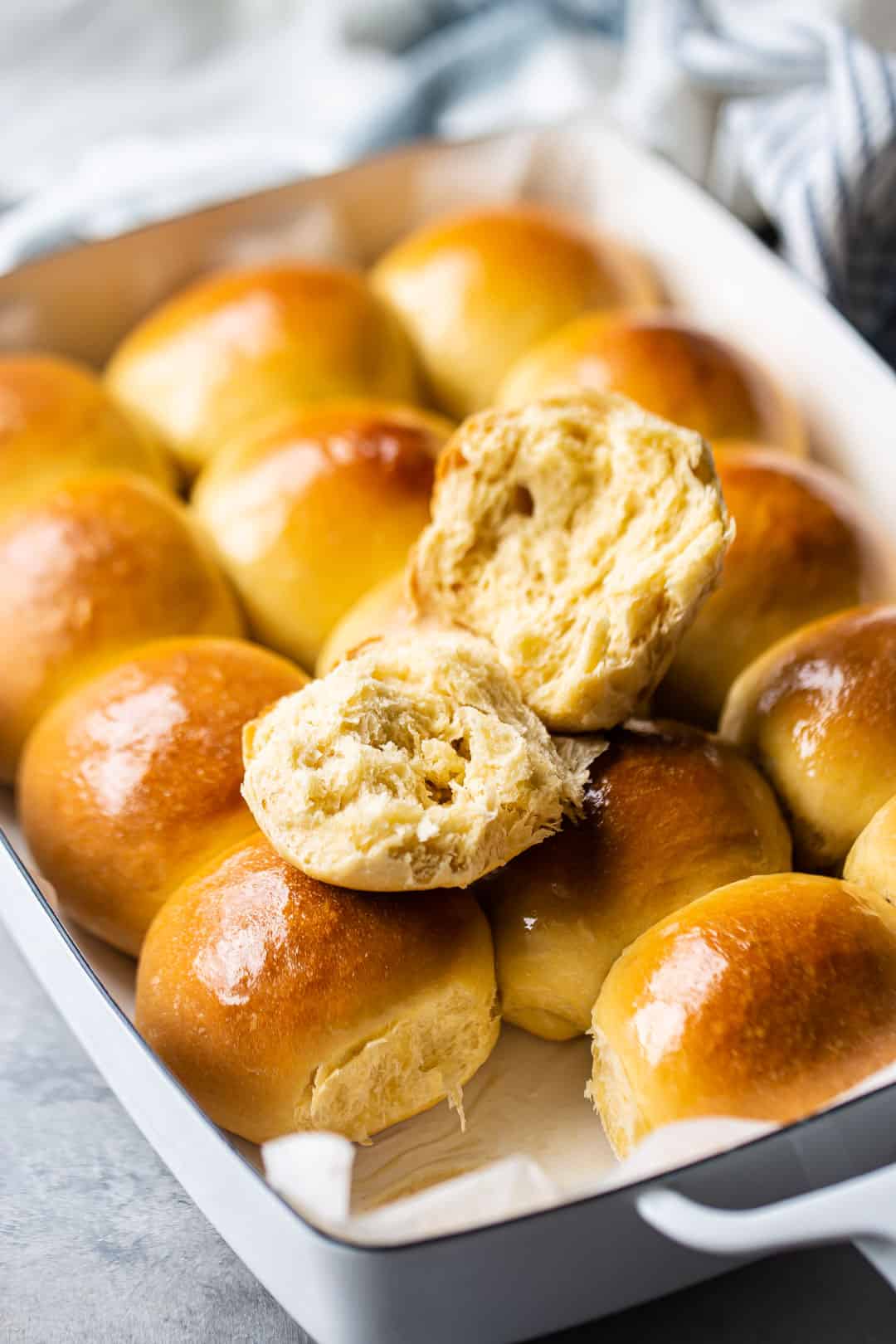 Hawaiian bread rolls in a pan with one roll split open so you can see the fluffy texture inside.