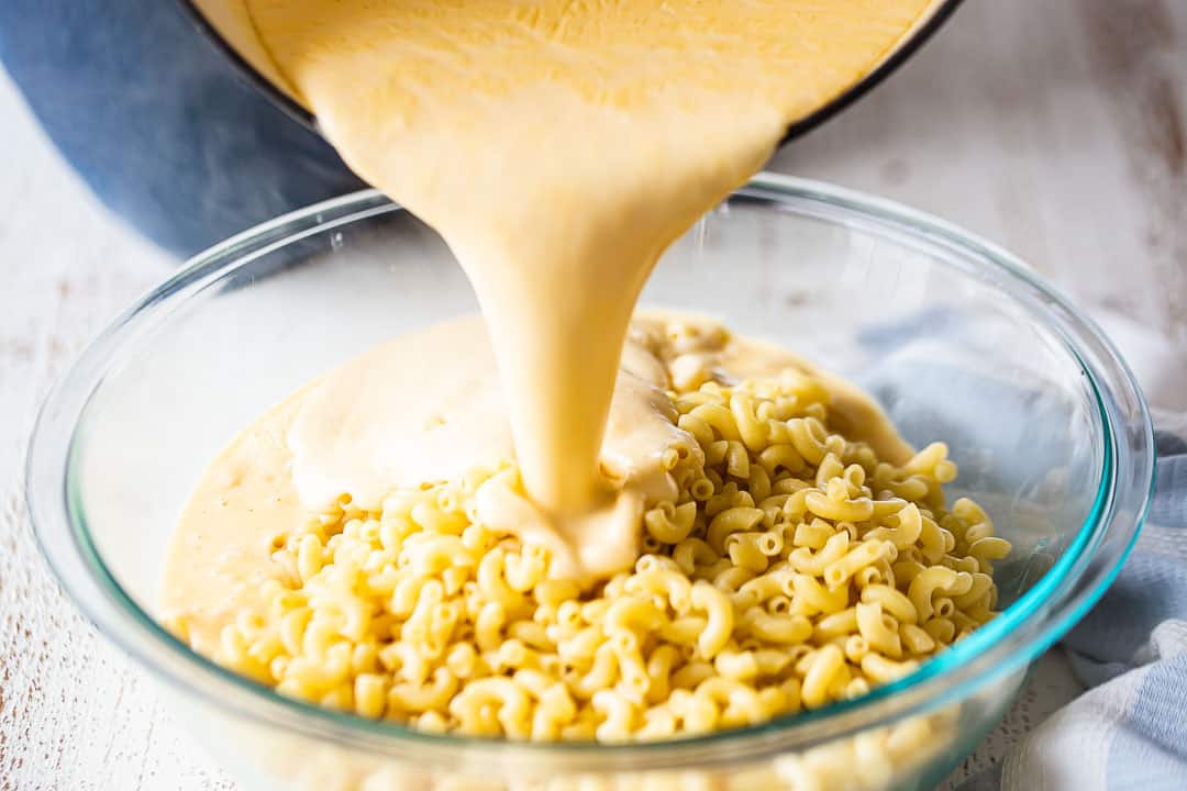 Pouring cheese sauce over cooked macaroni.