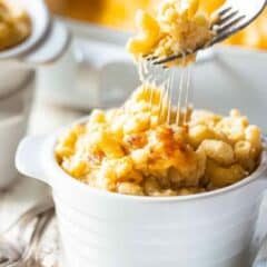 A fork pulling macaroni and cheese out of an individual ramekin, stretching the gooey cheese along with it.