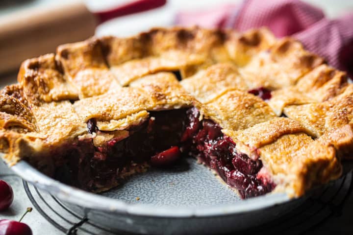 Sweet cherry pie recipe baked in a metal tin with slices taken out, showing the layers of flaky pie crust and chunky filling.