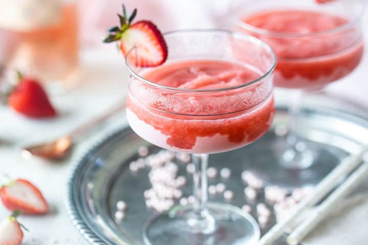 Frosé rosé in wine glasses on a vintage silver tray with fresh strawberries in the background.