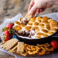 Dipping a graham cracker into s'mores dip baked in a skillet.