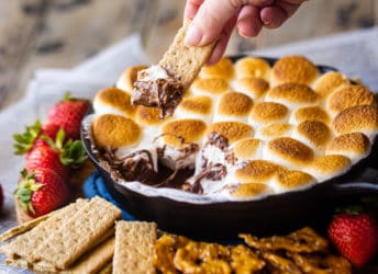 Dipping a graham cracker into s'mores dip baked in a skillet.