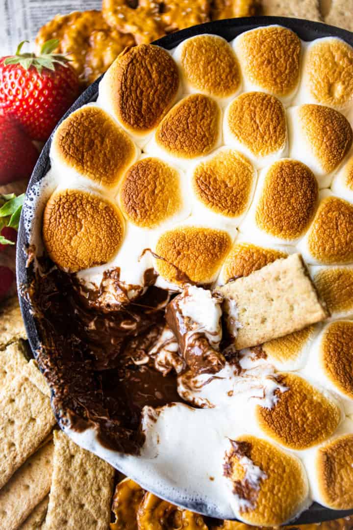 Close up image of s'mores dip with melted chocolate, toasted marshmallows, and graham crackers.