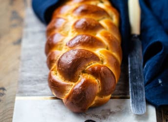 Challah bread on a marble board with a blue cloth.