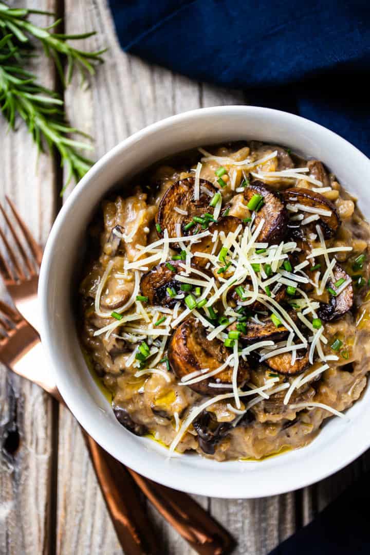 Overhead image of a bowl of vegan mushroom risotto on a rustic wooden background, with a blue linen napkin and copper fork.