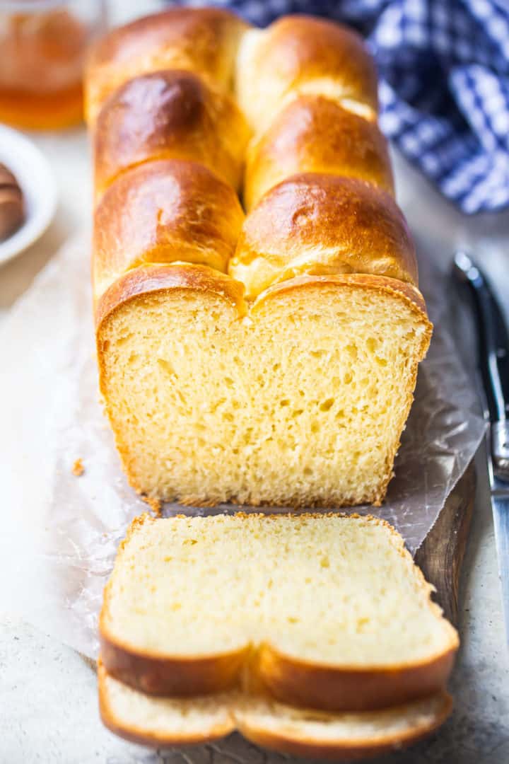 Brioche recipe, prepared, baked, and sliced with a blue checked cloth in the background.