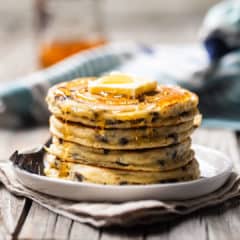 Chocolate chip pancakes with butter and syrup on a white plate.