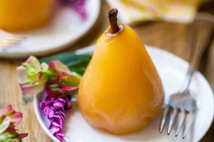 Poached pear on a plate with a vintage silver fork and a floral garnish.