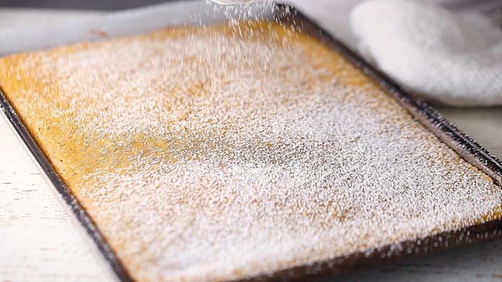 Dusting pumpkin roll cake with powdered sugar to prevent sticking.