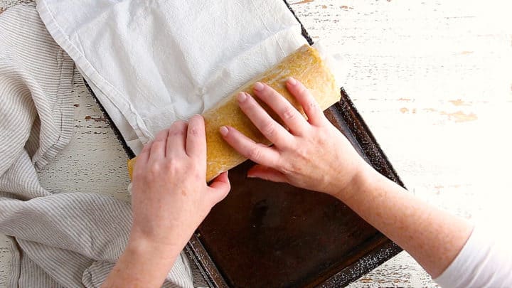 Rolling freshly baked pumpkin roll cake with a towel to prevent cracking.