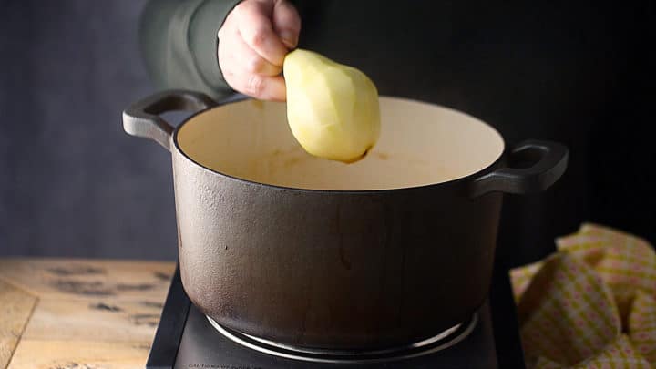 Adding peeled pears to a pot of poaching liquid.