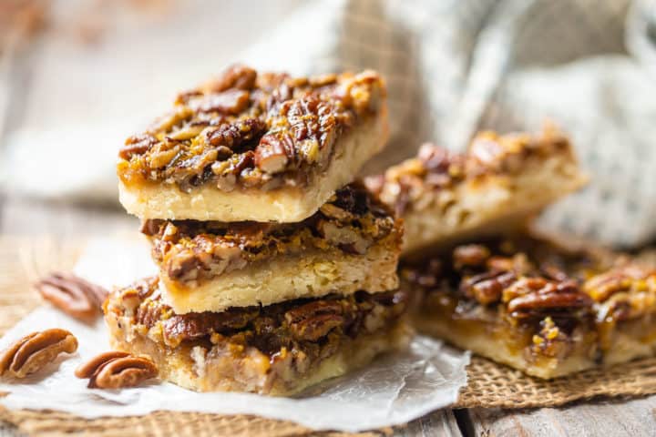 Best pecan pie bars arranged in stacks on burlap squares, with a green checked cloth in the background.