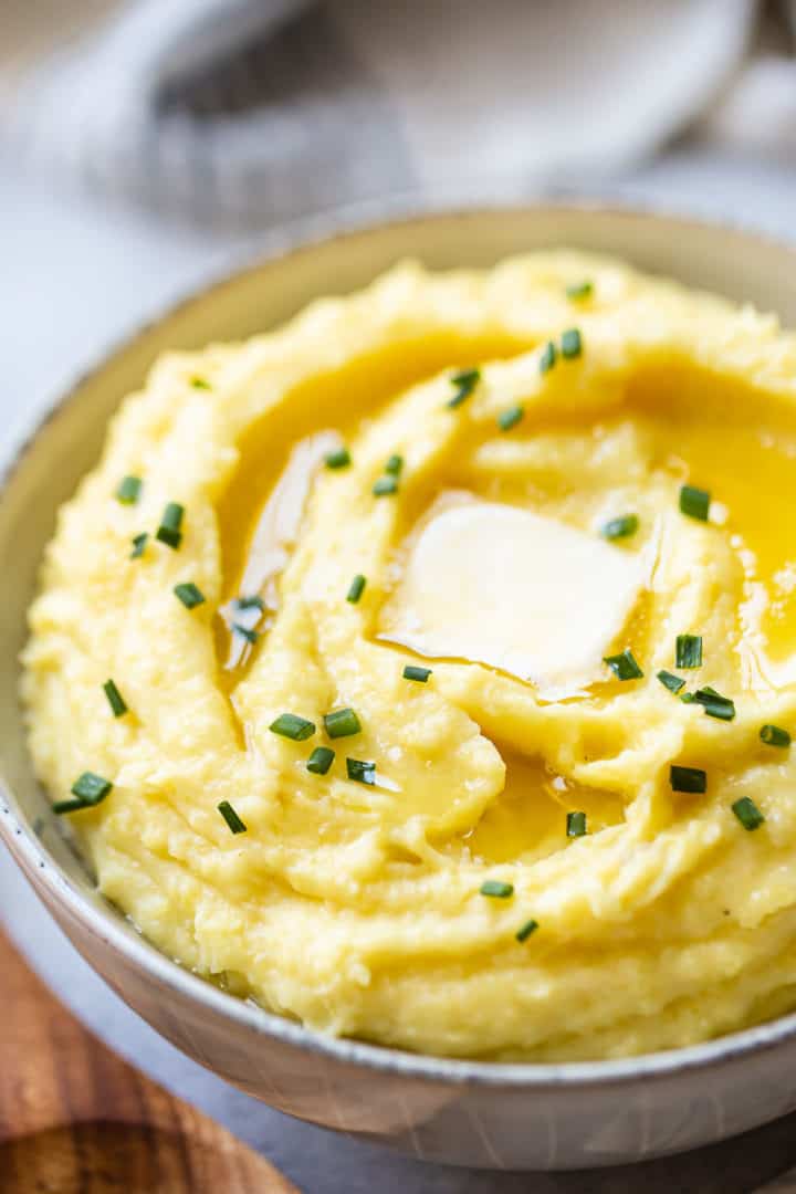Close-up image of mashed potato recipe, prepared and presented in a stoneware bowl and garnished with fresh chives.