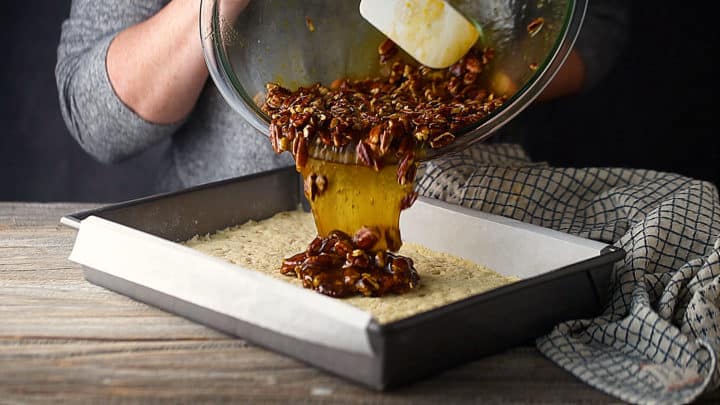 Pouring pecan pie filling over a partially baked shortbread crust.